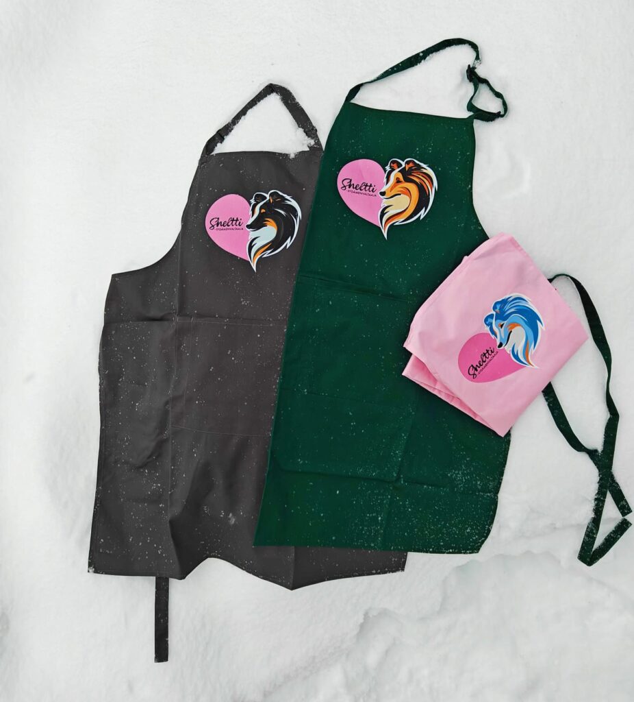 Essu taskulla. Helppo EasyCare-materiaali: 65% polyester, 35% puuvillatwill (195g/m²) . Pit. 86cm, lev. 72cm. 90cm solmimisnauhat sekä säädettävä niskanauha (pituus 70cm). Etutaskussa kynätasku. Pesu 60°C. Soopelikuva vain vihreään essuun,. Essun värit t.harmaa, t.vihreä ja pinkki. Kuvien värit: tricolour (musta), soopeli (ruskea) ja merle (sin.).